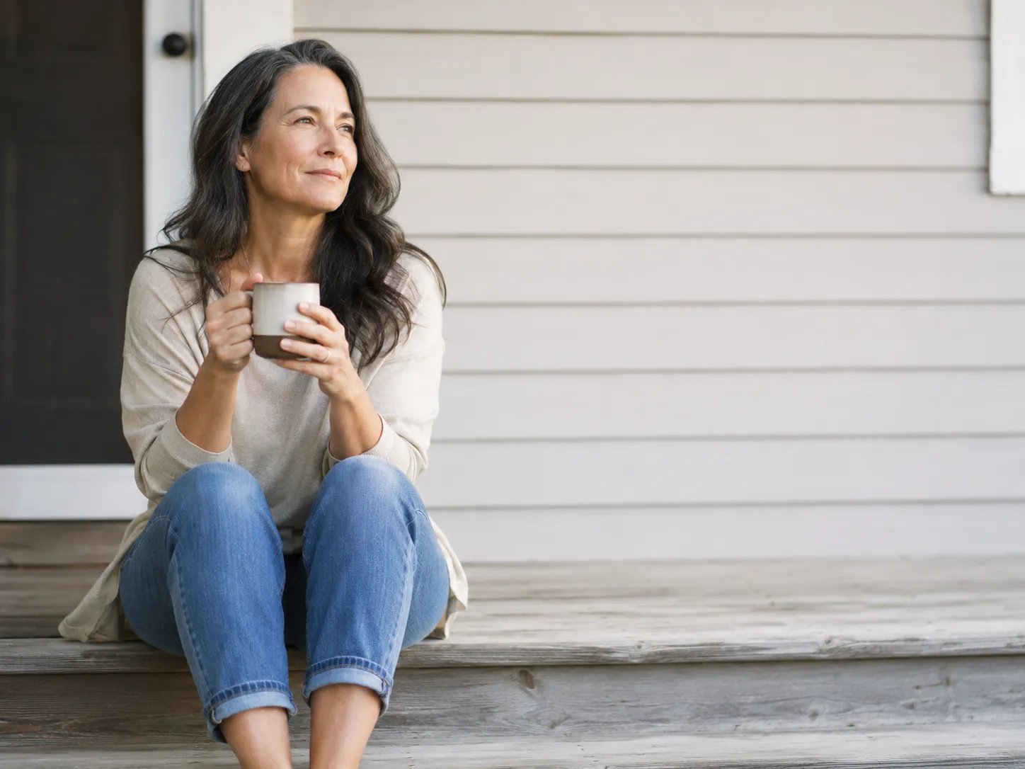 Woman in her 50s relaxing on porch with coffee morning light