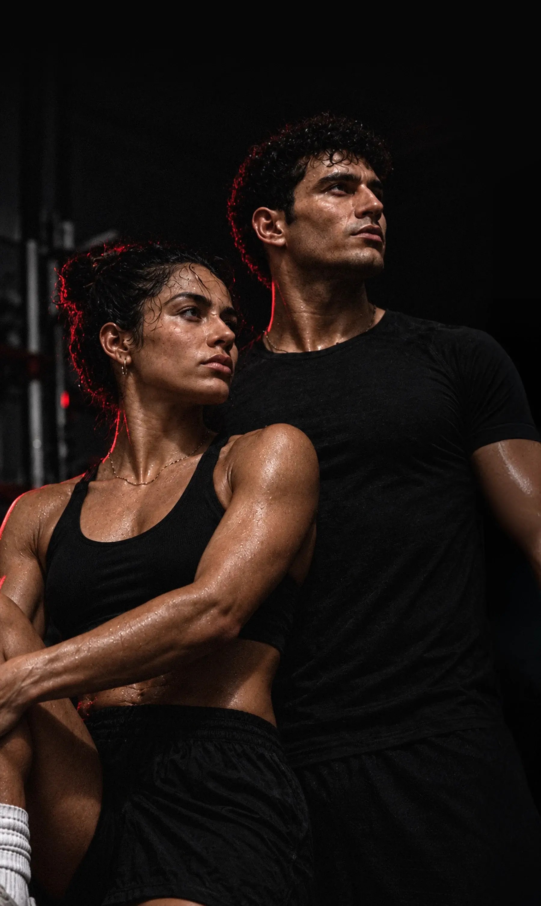 Man and woman in black athletic wear in a gym lit by red neon
