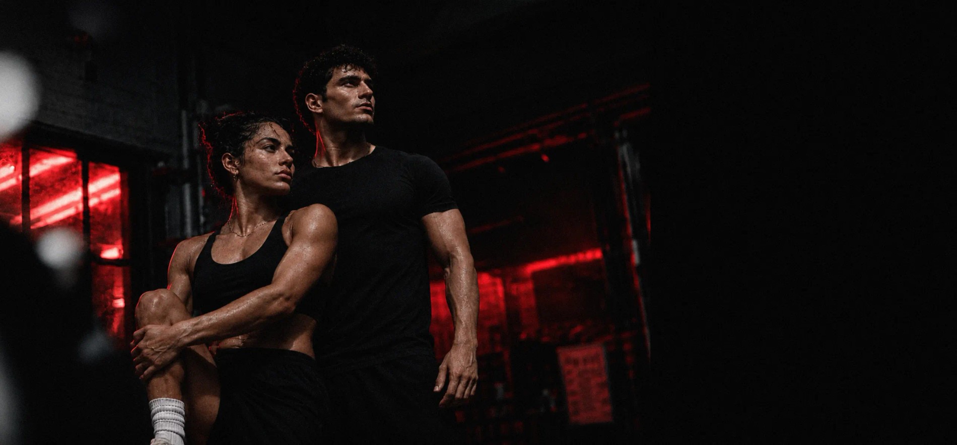 Man and woman in black athletic wear in a gym lit by red neon